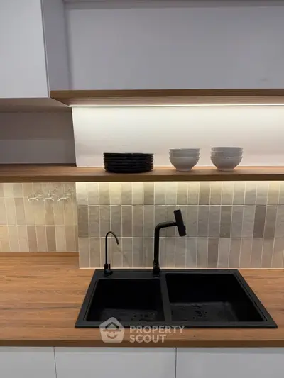 Modern kitchen with sleek black sink and wooden countertop, featuring stylish backsplash and under-cabinet lighting.