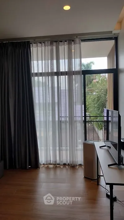 Modern living room with large window and balcony view, featuring sleek furniture and natural light.