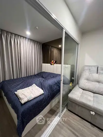 Cozy bedroom with modern decor and sliding glass partition, featuring a plush bed and stylish sofa.