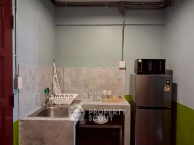 Compact kitchen with modern appliances and minimalist design, featuring a sleek countertop and stainless steel fridge.