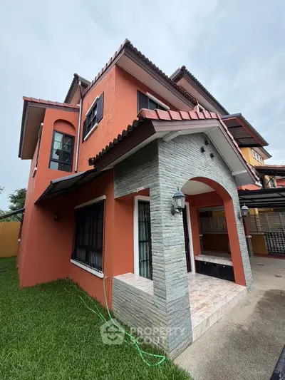 Charming two-story house with red exterior and lush green lawn, perfect for family living.