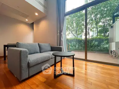 Spacious living room with modern sofa and large glass doors opening to a lush balcony view.