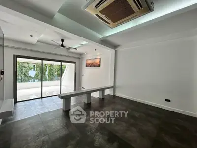 Spacious modern living room with large sliding glass doors leading to a balcony, featuring sleek flooring and ceiling fan.