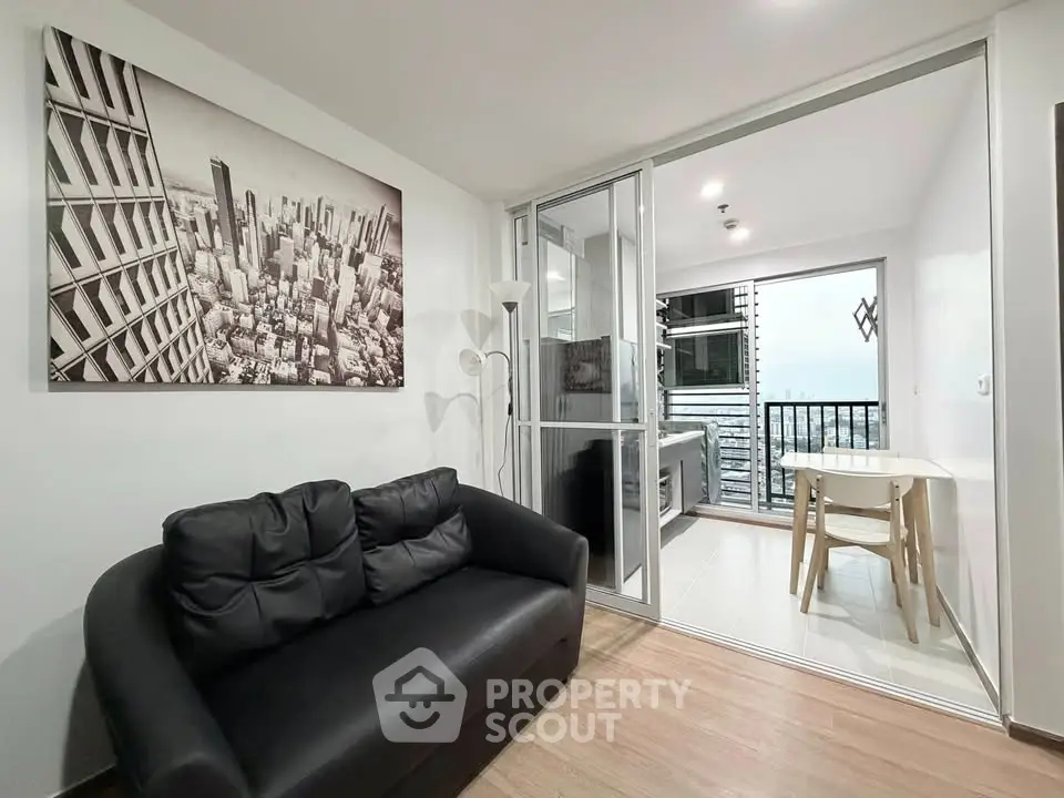 Modern living room with black sofa and cityscape artwork, leading to a bright balcony with a stunning view.