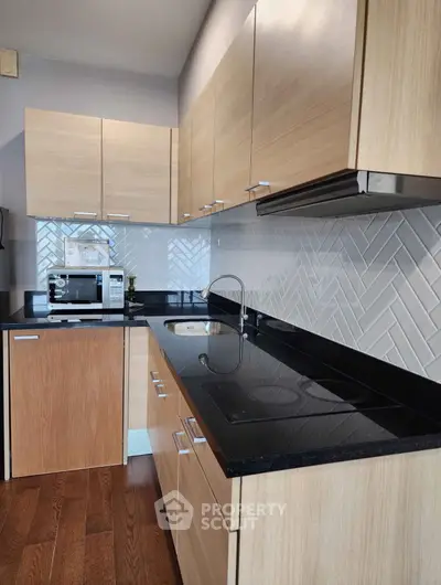 Modern kitchen with sleek black countertops and light wood cabinets, featuring a built-in microwave and electric stove.