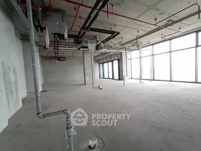 Spacious unfinished commercial space with large windows and exposed pipes, ideal for customization.