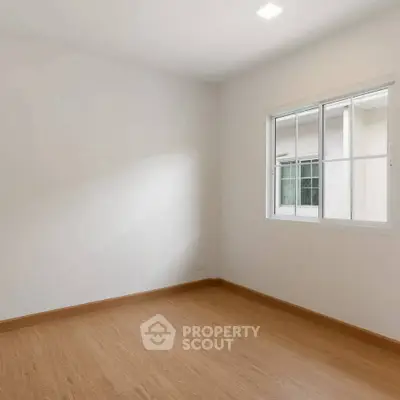 Spacious empty room with wooden flooring and large window, perfect for customization.