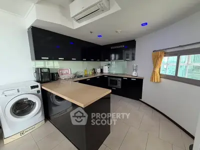 Modern kitchen with sleek black cabinets, integrated appliances, and a washing machine, offering a stylish cooking space.