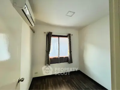 Cozy bedroom with wooden flooring and air conditioning, featuring a window with curtains for natural light.