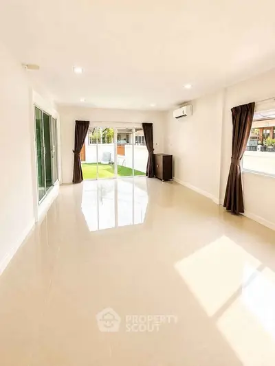 Spacious sunlit living room with large windows and garden view, perfect for modern living.