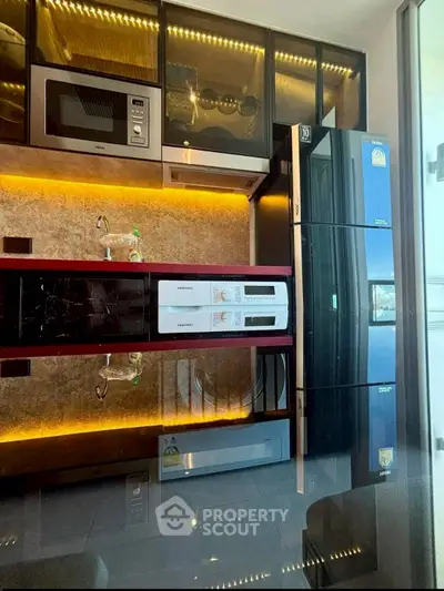 Modern kitchen with sleek appliances and ambient lighting, featuring a fridge, microwave, and washing machine.