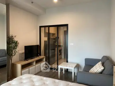 Modern living room with sleek furniture and glass partition leading to kitchen.