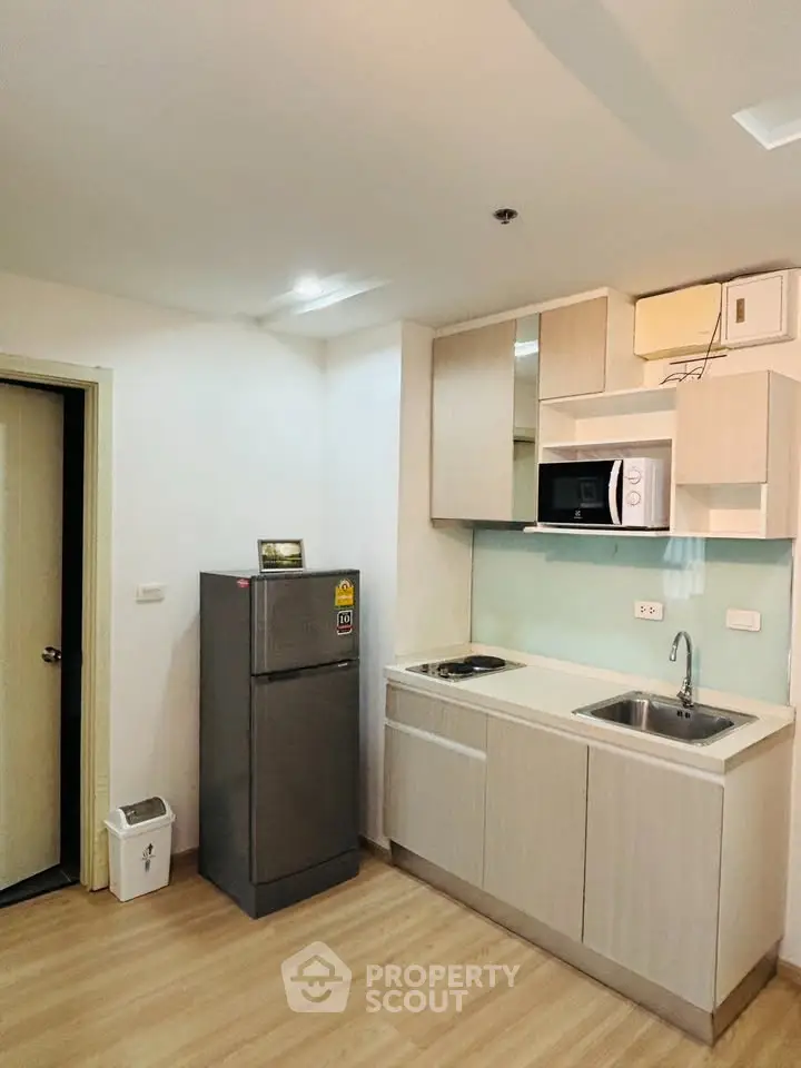 Modern kitchen with sleek cabinetry, compact fridge, and built-in microwave in a cozy apartment.