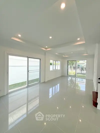 Spacious modern living room with large windows and glossy tiled floors, offering abundant natural light.