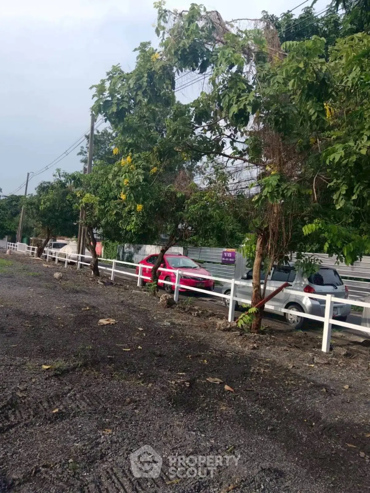 Spacious parking area with lush greenery and secure fencing, ideal for residential or commercial use.