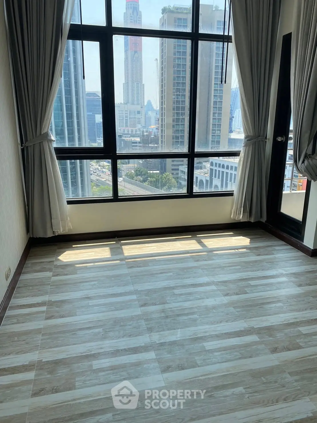 Spacious room with large windows offering stunning city views in a modern high-rise building.