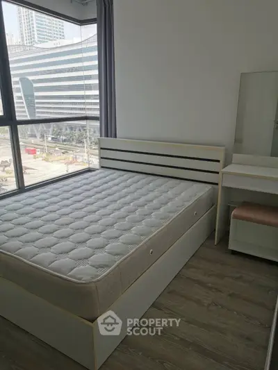 Modern bedroom with large window and city view, featuring a stylish bed and vanity set.