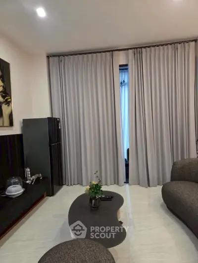 Modern living room with elegant curtains and stylish furniture, featuring a sleek black refrigerator and chic decor.