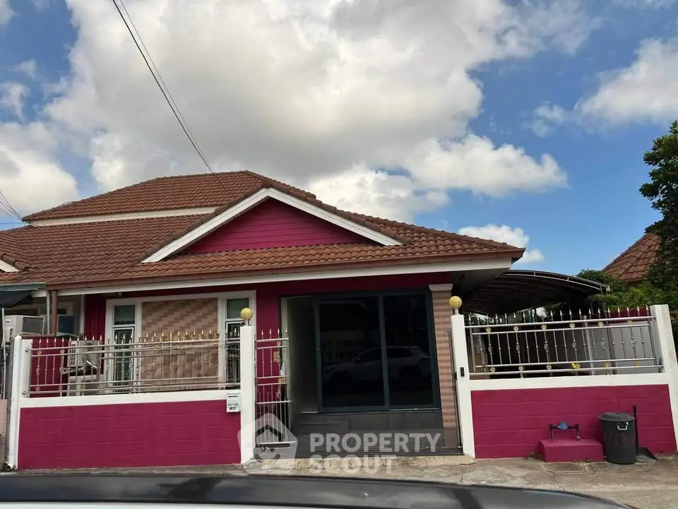 Charming single-story house with vibrant pink exterior and tiled roof, featuring a gated entrance and spacious driveway.