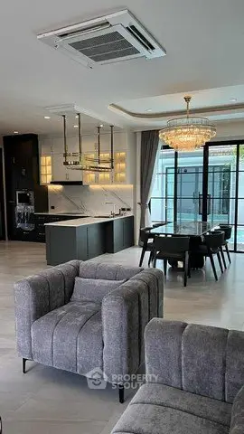 Luxurious open-plan living room with modern kitchen and elegant dining area, featuring stylish gray furniture and chandelier.