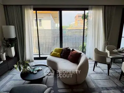Stylish modern living room with cozy seating and large windows offering natural light and a view of the balcony.