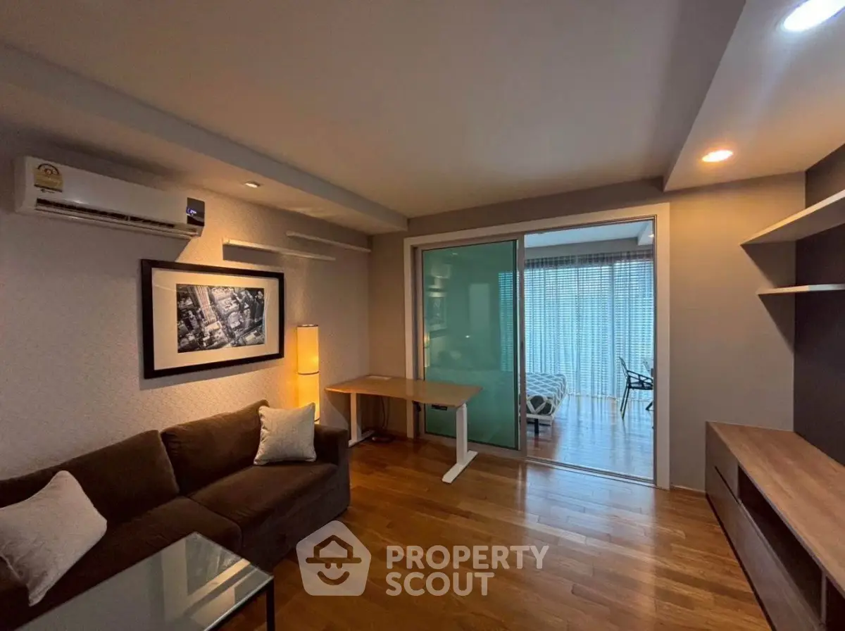 Modern living room with wooden flooring and sliding glass doors leading to a balcony.