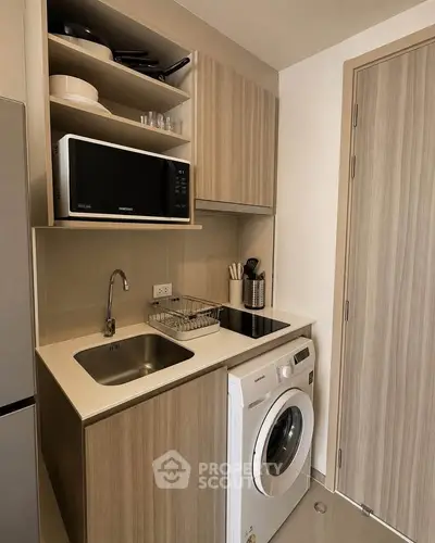 Compact modern kitchen with washing machine and microwave in stylish apartment.