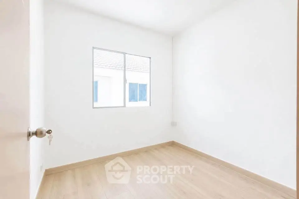 Bright empty bedroom with wooden flooring and large window in modern apartment.