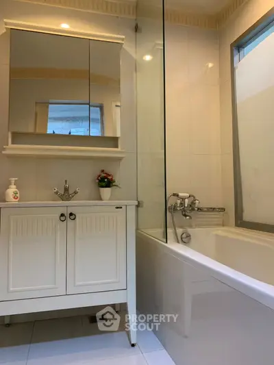 Modern bathroom with sleek white vanity and bathtub, featuring elegant fixtures and ample natural light.