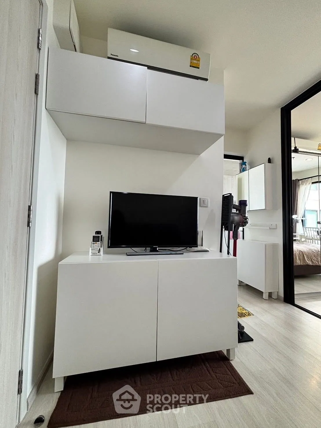Modern living room with sleek white furniture and TV, showcasing minimalist design and cozy ambiance.