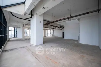 Spacious industrial-style open floor plan with large windows and exposed pipes, ideal for creative workspace.