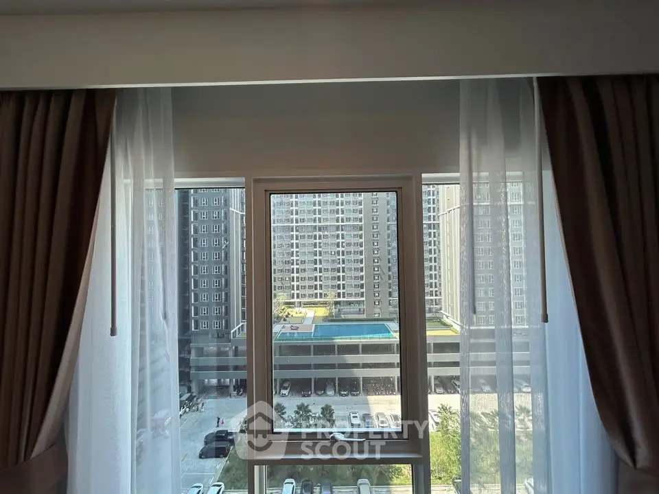 Stunning view from apartment window overlooking modern building and pool area.