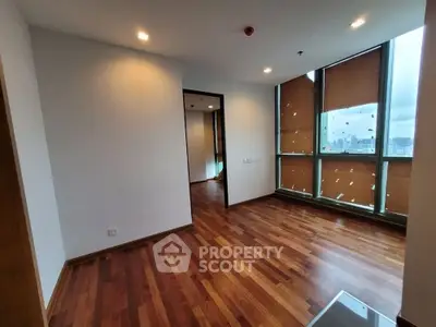 Spacious empty room with wooden flooring and large windows offering city views.