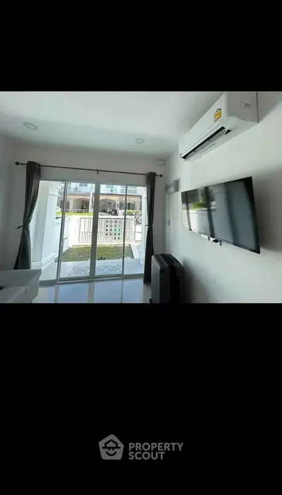 Modern living room with large TV and air conditioning, featuring sliding glass doors to a balcony.