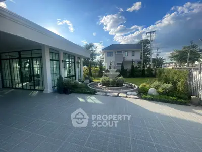 Stunning modern home with spacious garden and elegant fountain under a clear blue sky.