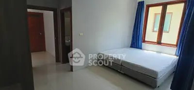 Bright bedroom with twin beds and large window, featuring blue curtains and minimalist decor.