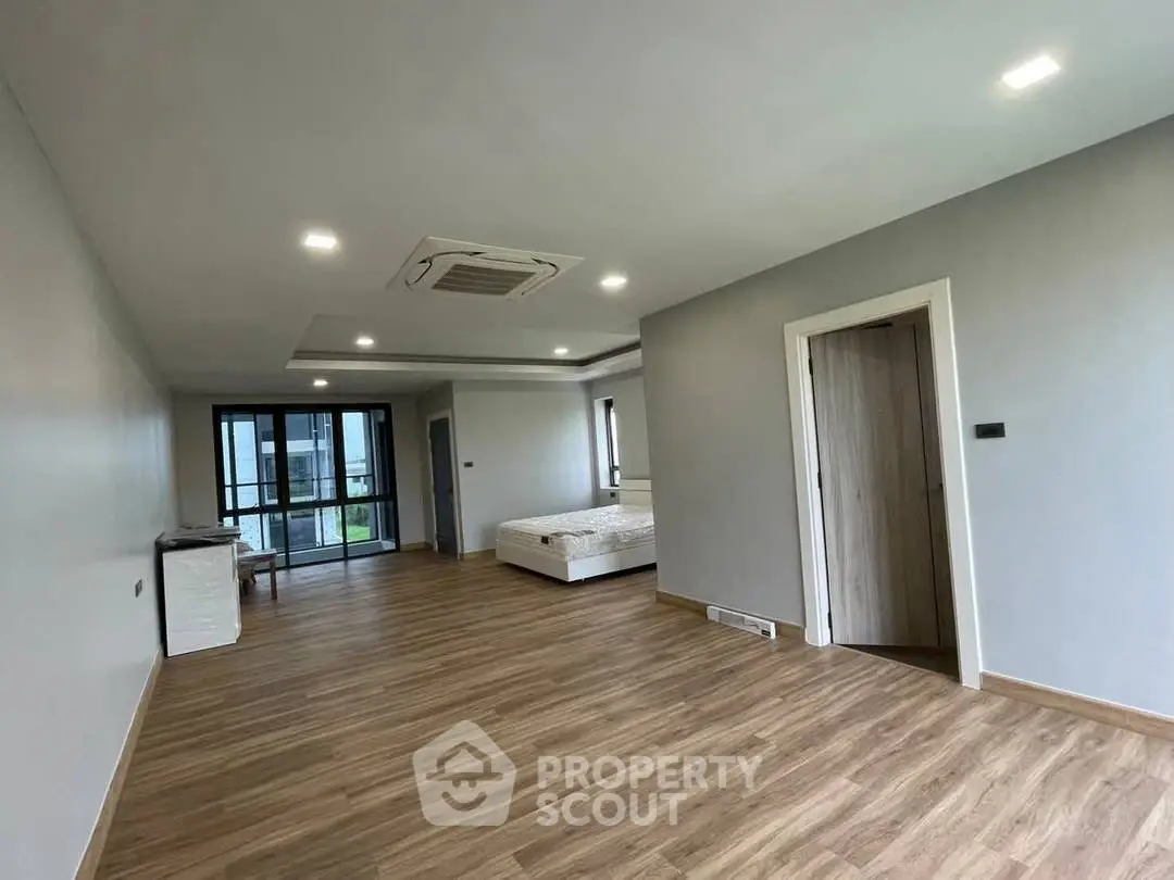 Spacious modern bedroom with wooden flooring and large windows in a luxury apartment.