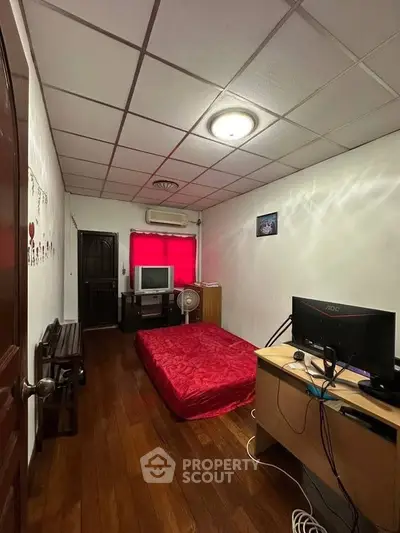 Cozy bedroom with wooden flooring, red accents, and a compact workspace setup.