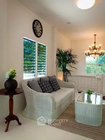 Charming living room with wicker furniture and elegant decor, featuring large windows and lush greenery.