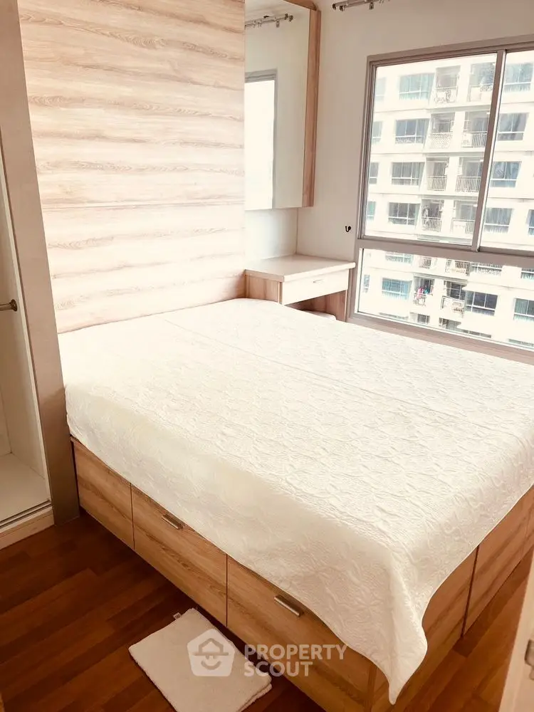 Cozy bedroom with wooden flooring and large window offering city view.