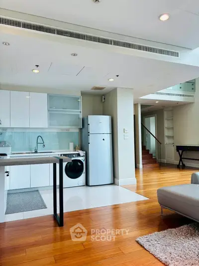 Modern open-plan living room with sleek kitchen and wooden flooring in a stylish apartment.