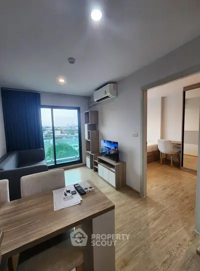 Modern living room with wooden flooring, stylish furniture, and large window offering city views.