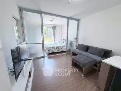 Modern living room with sliding glass doors leading to a bright bedroom, featuring sleek furniture and natural light.