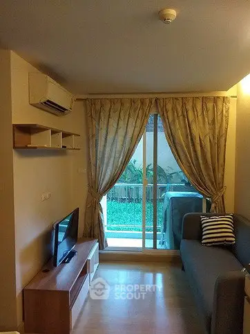 Cozy living room with sliding glass doors leading to a garden view balcony, featuring modern furniture and air conditioning.