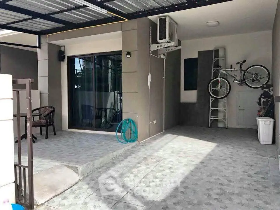 Modern home exterior with covered parking and patio area, featuring a bicycle and outdoor seating.