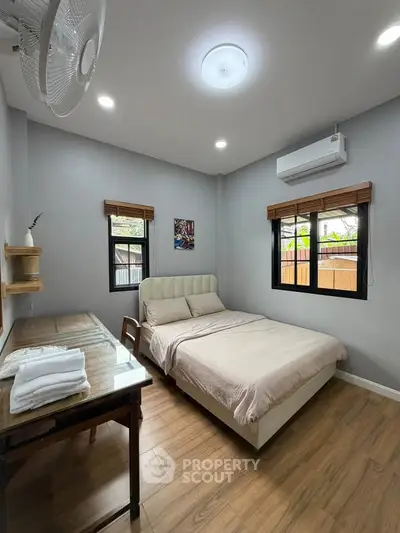 Cozy bedroom with modern decor, featuring a comfortable bed, wooden flooring, and ample natural light.