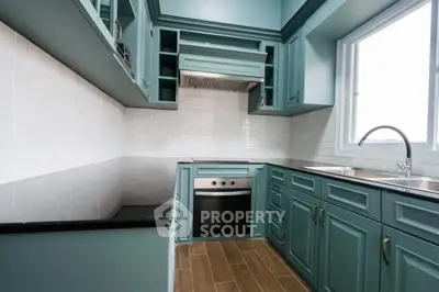 Modern kitchen with teal cabinetry, built-in oven, and large window for natural light.