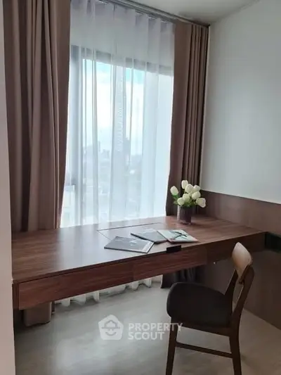 Modern study area with wooden desk and chair, featuring a large window with sheer curtains and a vase of flowers.