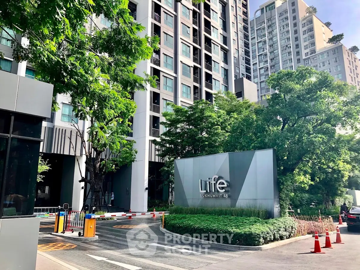 Modern condominium entrance with lush greenery and high-rise buildings in urban setting.