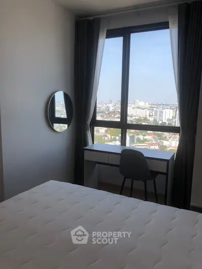 Modern bedroom with city view, featuring a stylish desk and round mirror.